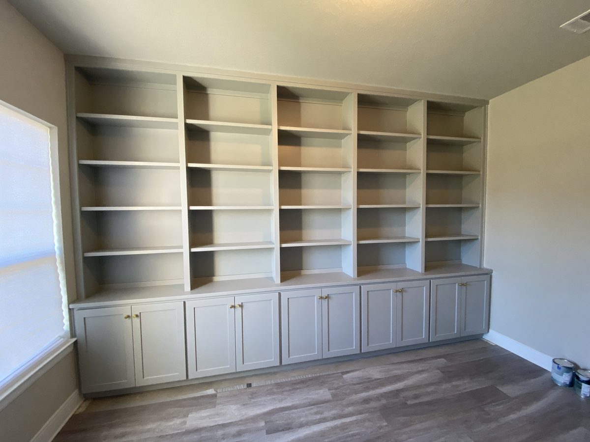 A full wall of custom built-in bookcases with adjustable shelves, painted cabinet bases and brass pulls.