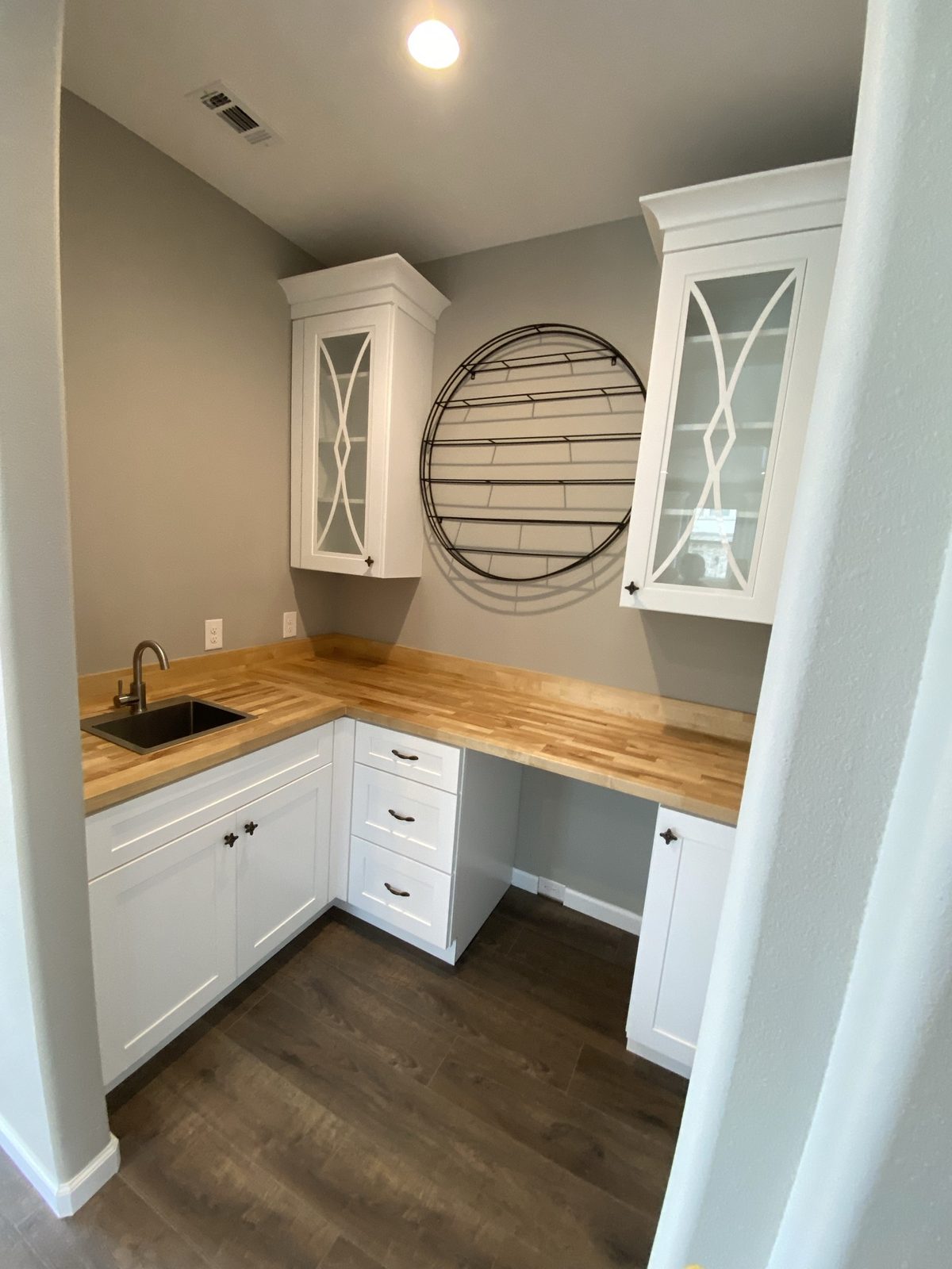 Coffee bar built into an alcove with butcher-block counter, a small sink, glass-front upper cabinets and drawer storage.