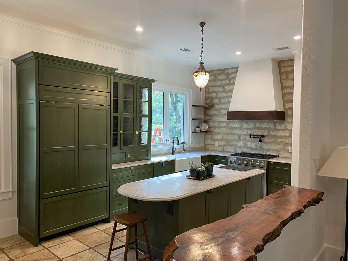 Custom kitchen with olive-green inset cabinetry, a panel-front refrigerator surround, a glass-front hutch and a live-edge wood bar top.