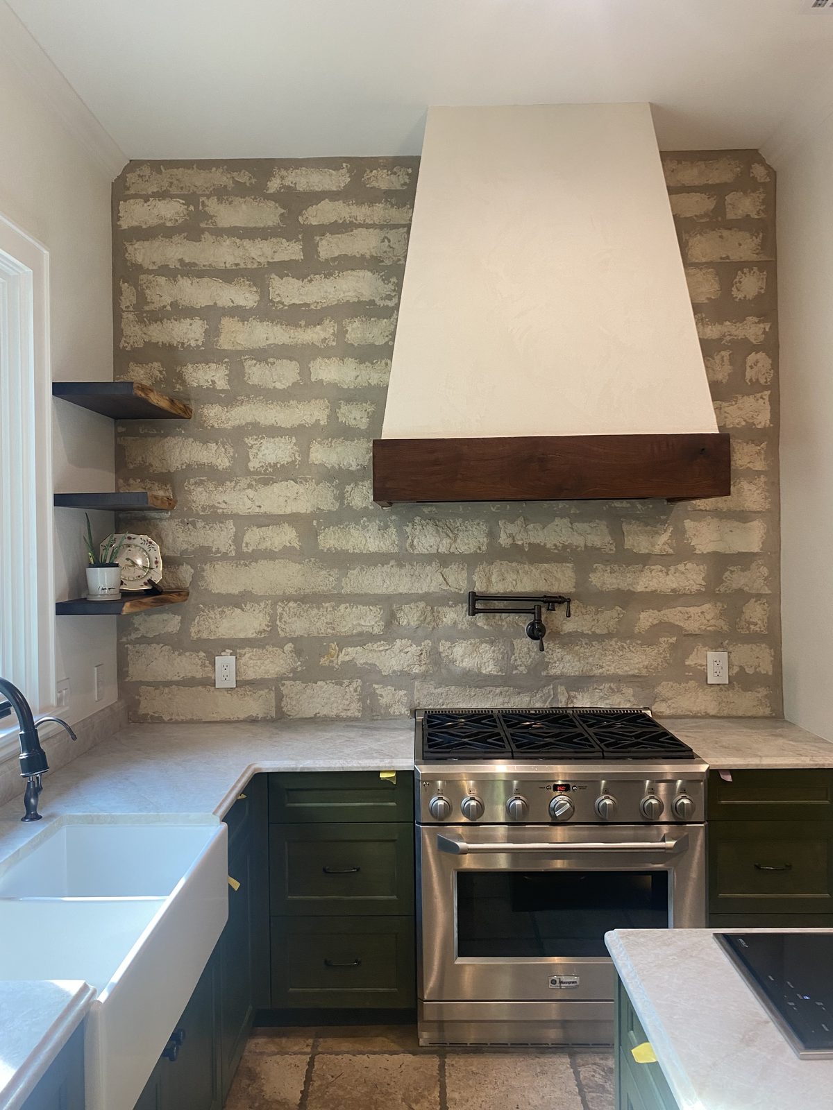 Plaster range hood with a solid wood band and floating wood shelves scribed to an uneven masonry wall.