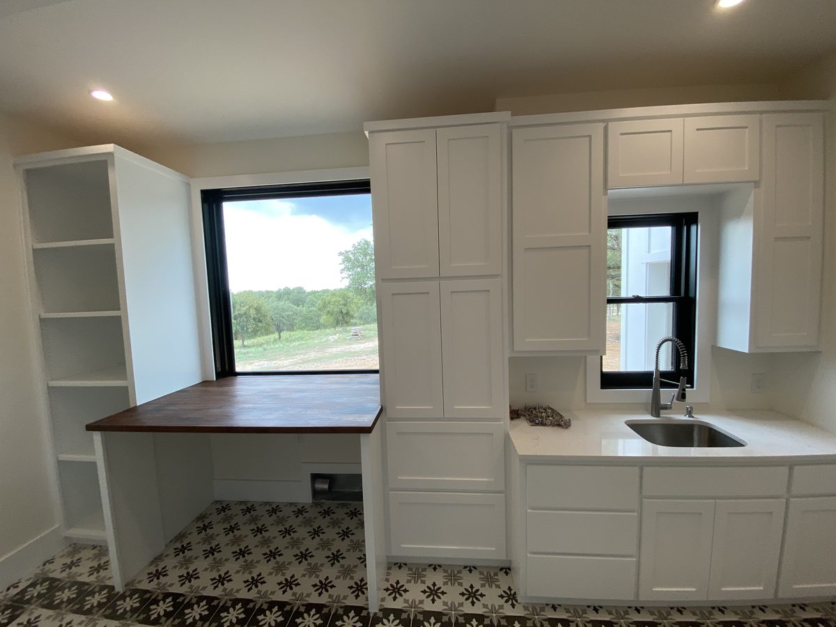 Utility room with floor-to-ceiling cabinetry, an open shelving tower and a built-in desk with a stained wood top.